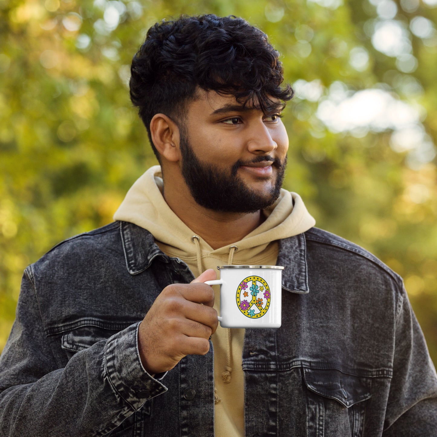 Person holding a white enamel mug with a pink, yellow, and blue peace sign graphic printed on the side to the right of the mug handle.