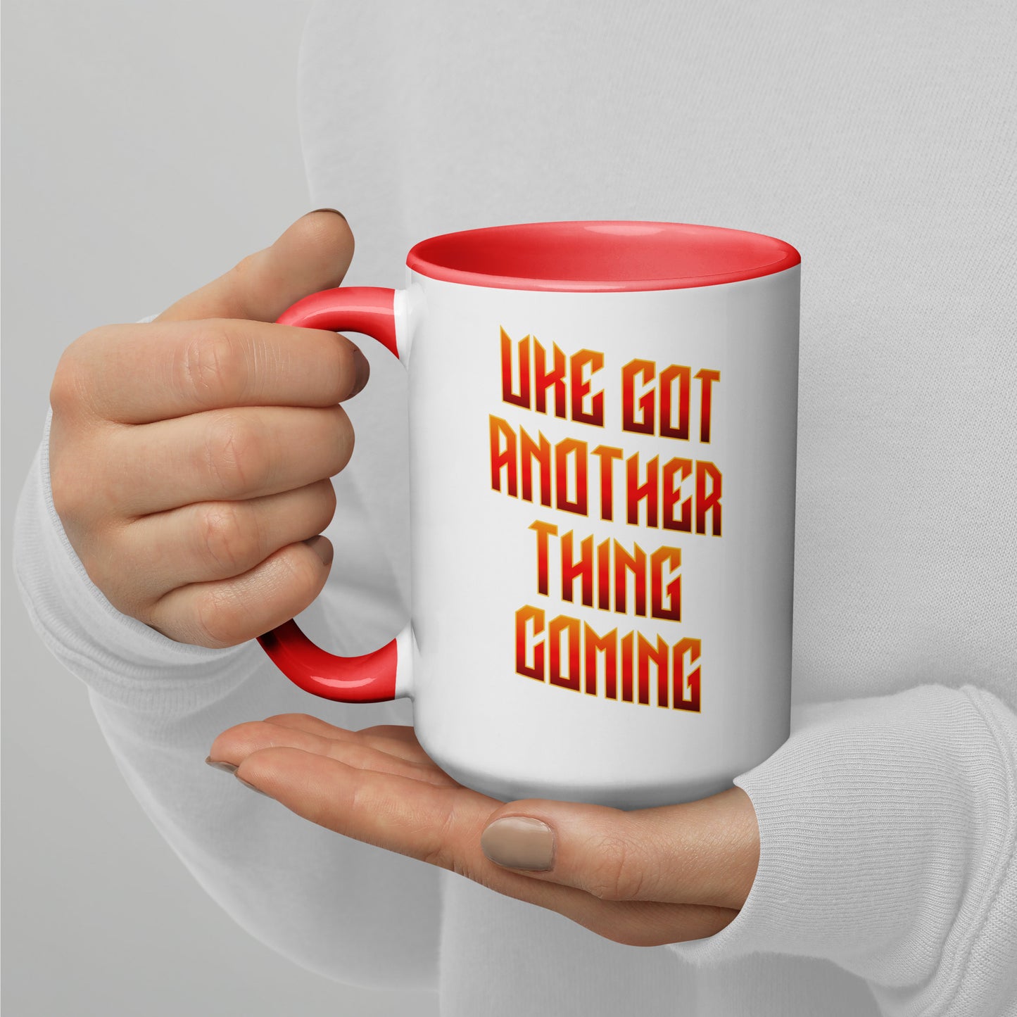 White mug with red handle and inside, with ‘Uke Got Another Thing Coming' in orange and yellow slanted block letters printed on the side to the right of the handle.
