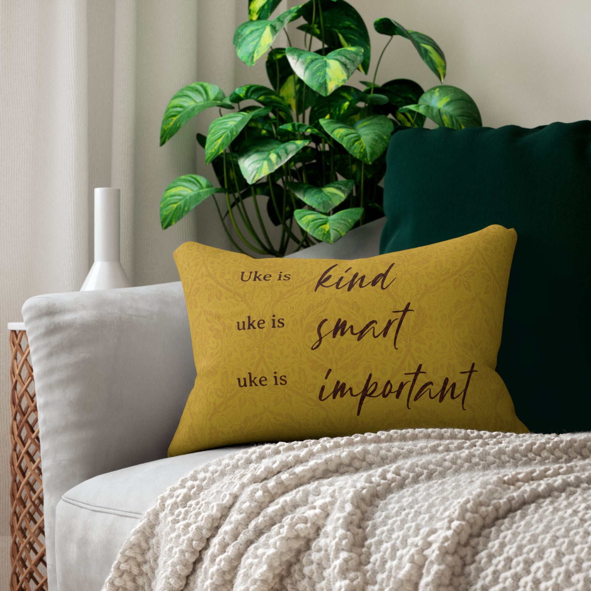 A throw pillow with a mustard-colored patterned background and 'Uke is kind, uke is smart, uke is important' printed on it, sitting on a sofa.