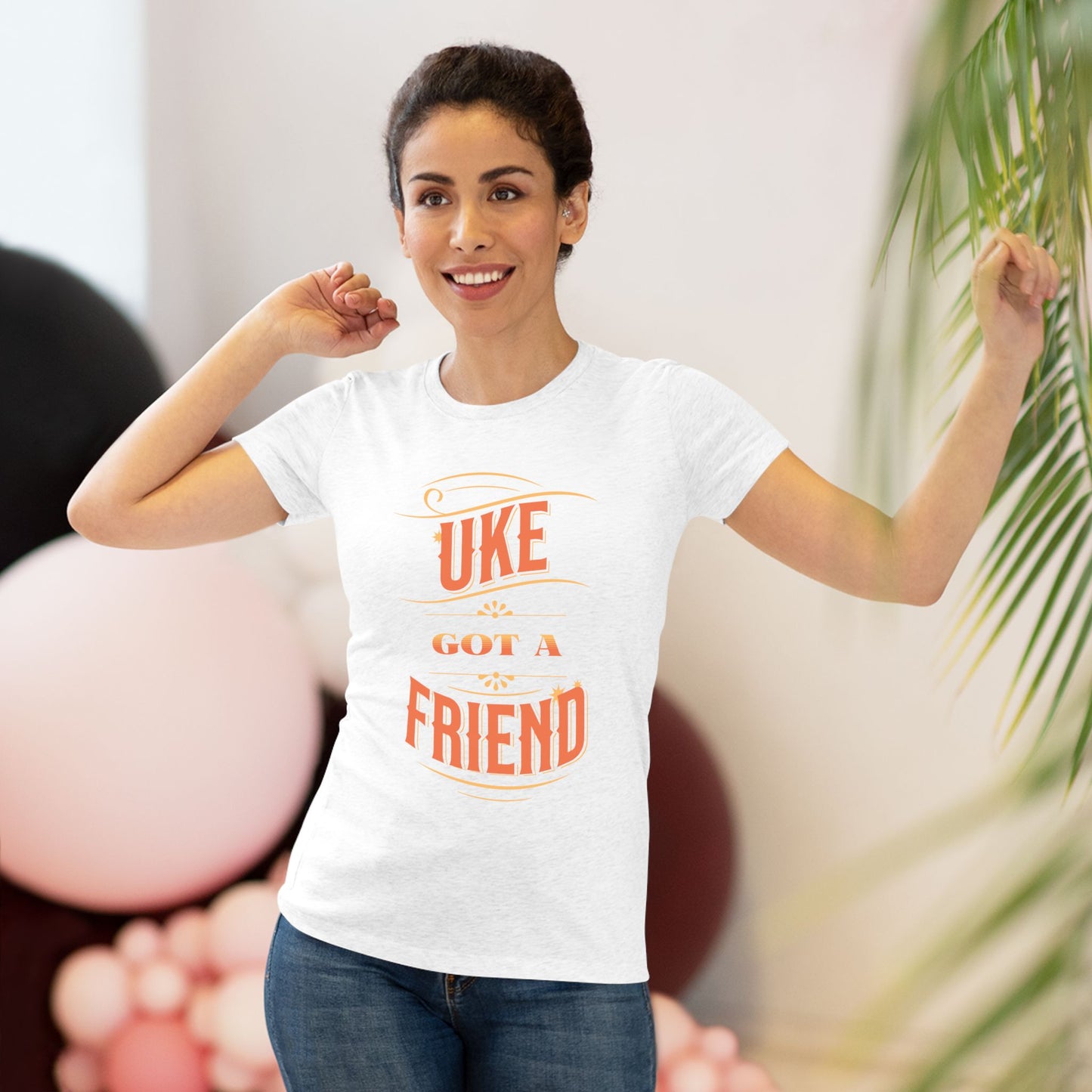 Woman wearing a heathered white t-shirt with ‘Uke Got A Friend' in orange and yellow block letters printed on it.