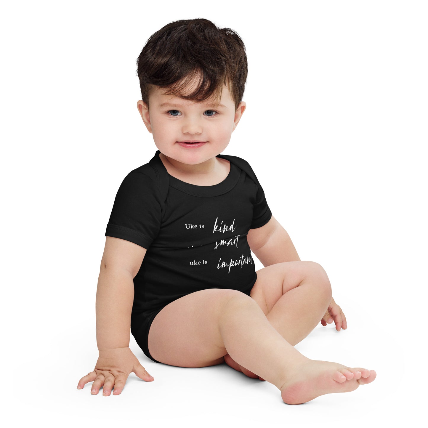 A baby wearing a black onesie printed with 'Uke is kind, uke is smart, uke is important' in white letters.