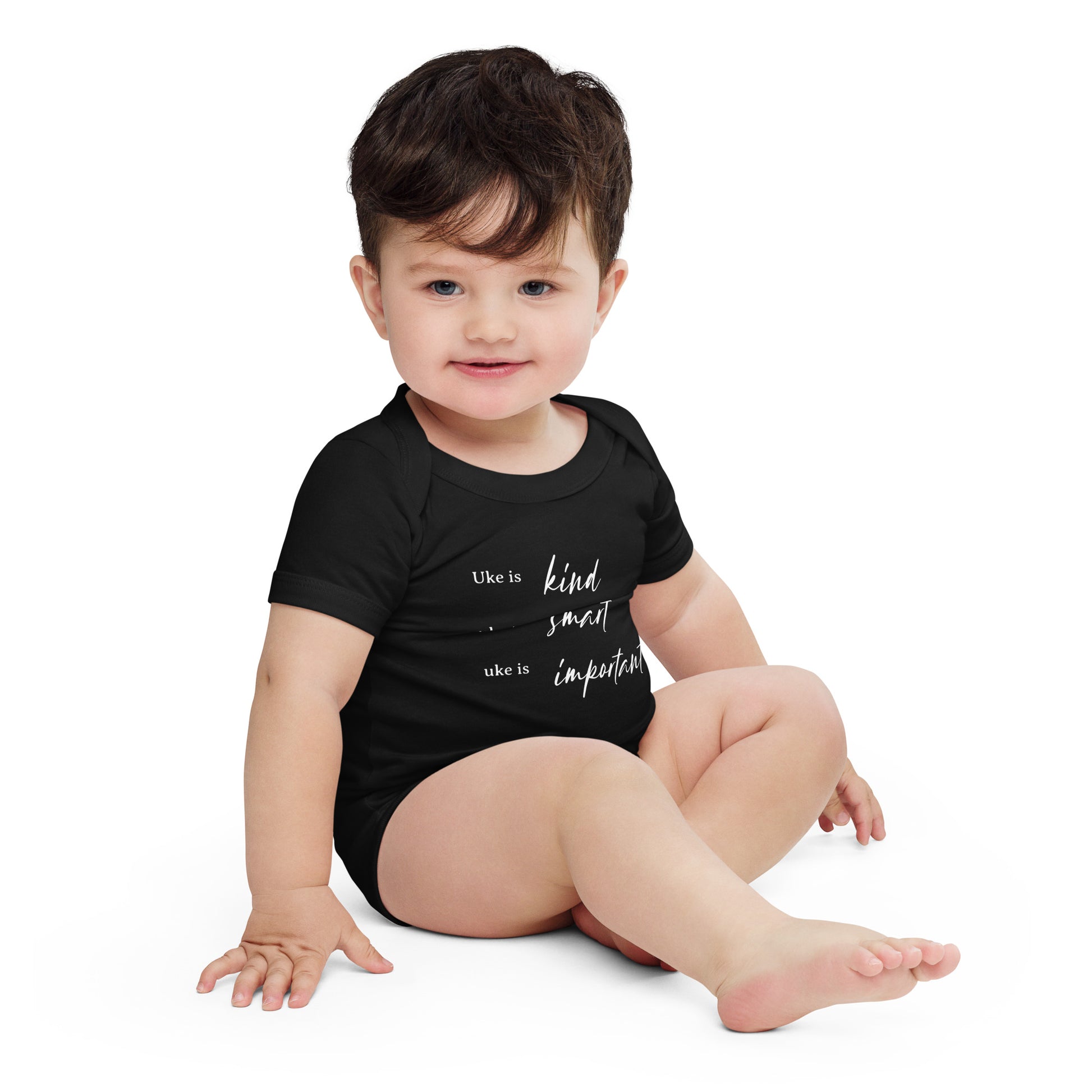 A baby wearing a black onesie printed with 'Uke is kind, uke is smart, uke is important' in white letters.