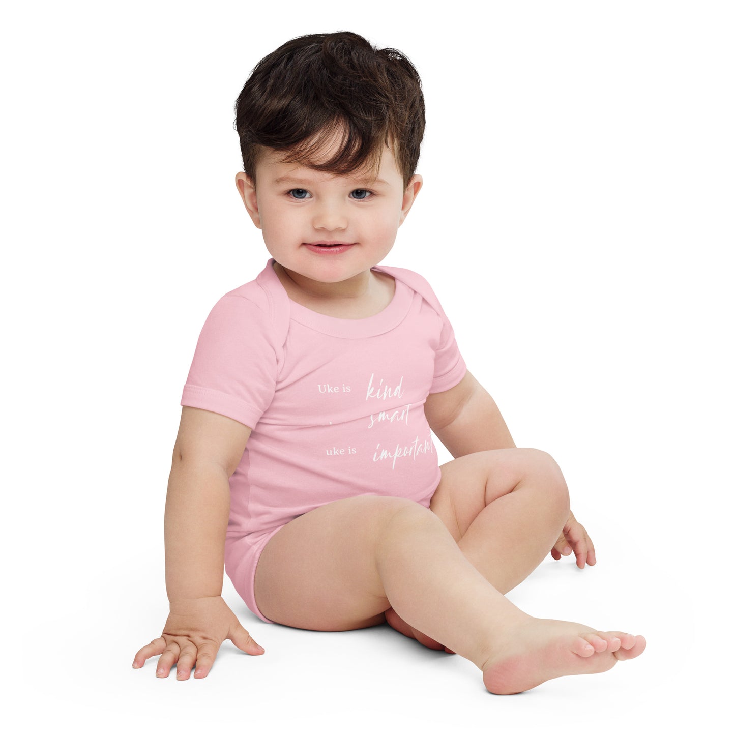 A baby wearing a light pink onesie printed with 'Uke is kind, uke is smart, uke is important' in white letters.