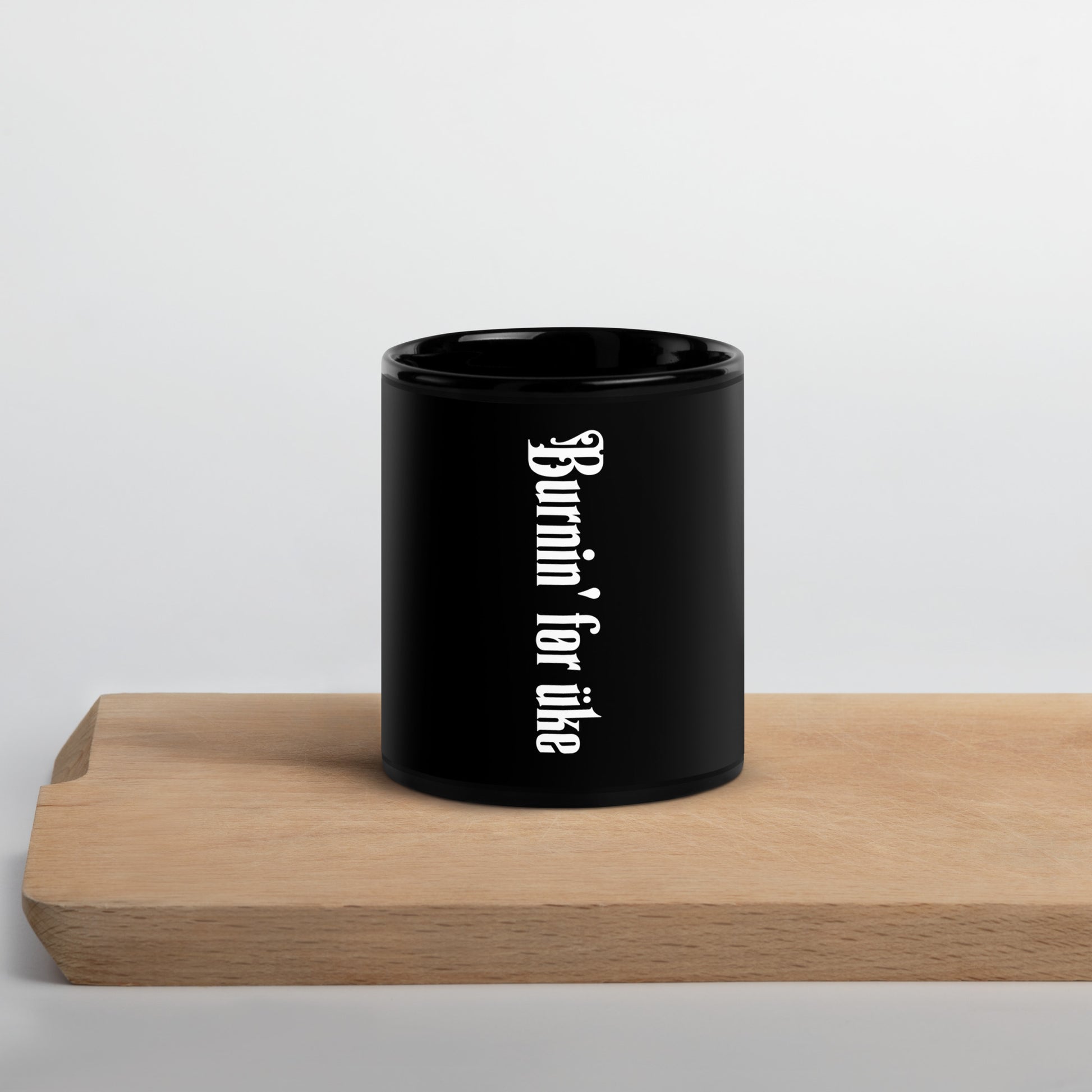 Glossy black mug with 'Burnin' for uke' in white Gothic letters printed vertically on the side opposite the handle.