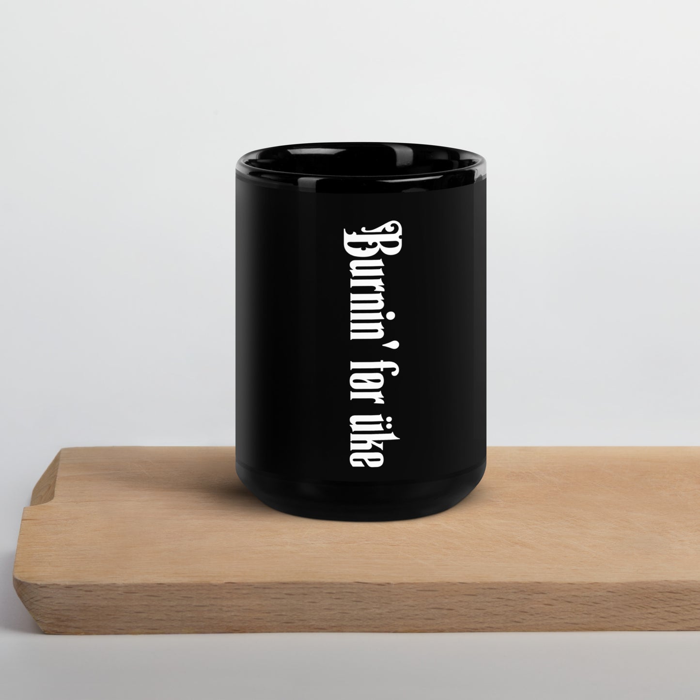 Glossy black mug with 'Burnin' for uke' in white Gothic letters printed vertically on the side opposite the handle.