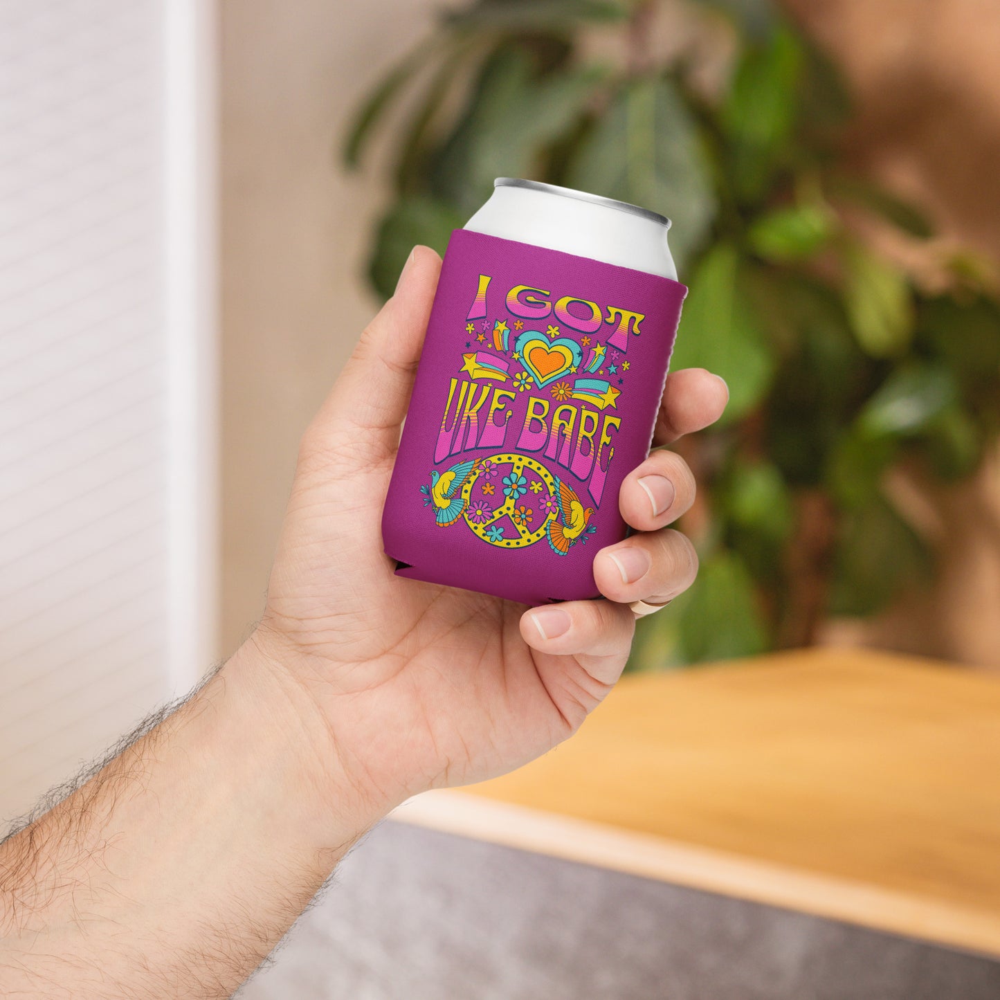 Hand holding a regular-sized can coozie with a deep pink background and a pink, blue, and yellow 'I Got Uke Babe’ and peace sign graphic printed on it.