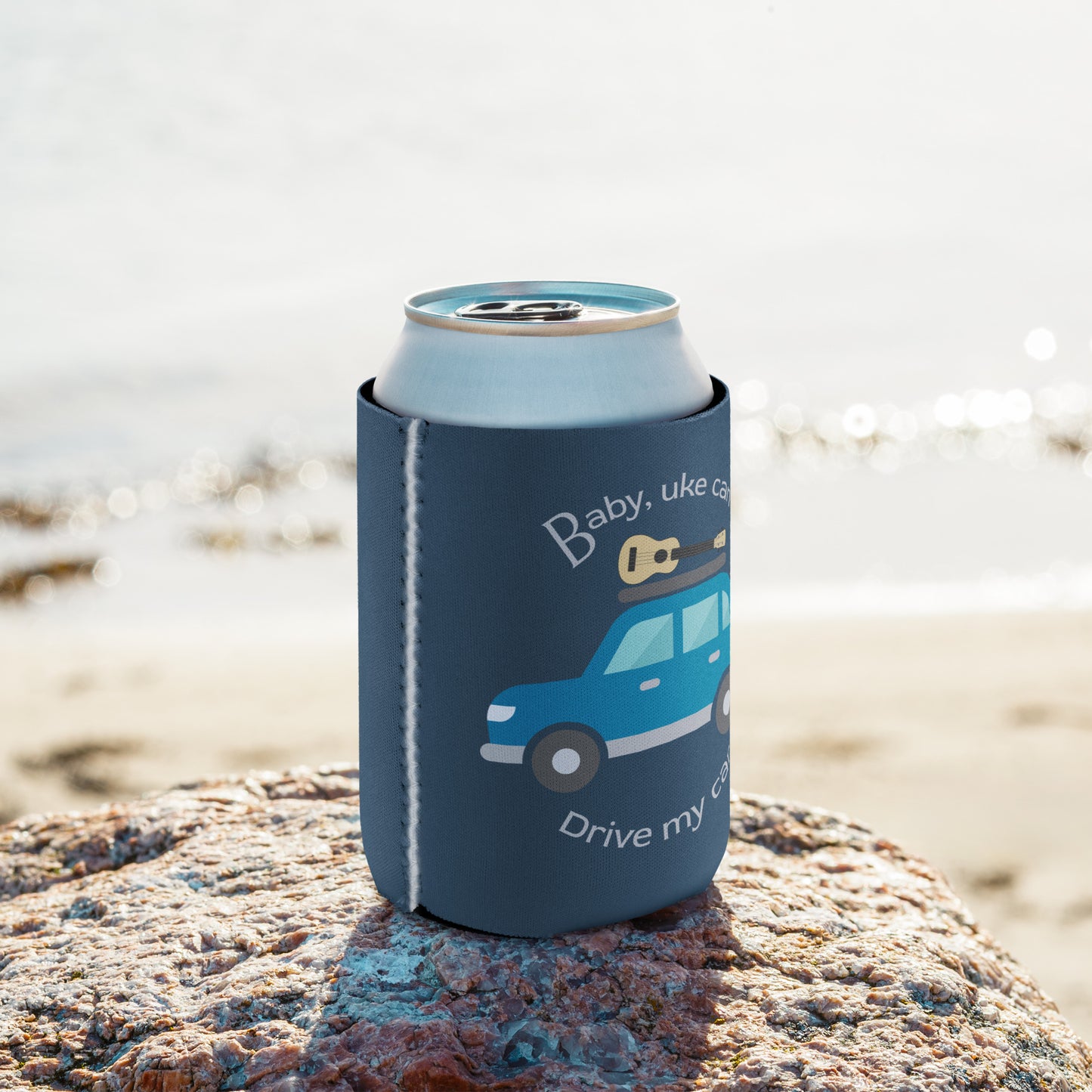 Regular-sized can coozie printed with an indigo background and ‘Baby, uke can drive my car’ with a graphic of a car with a ukulele on the roof.