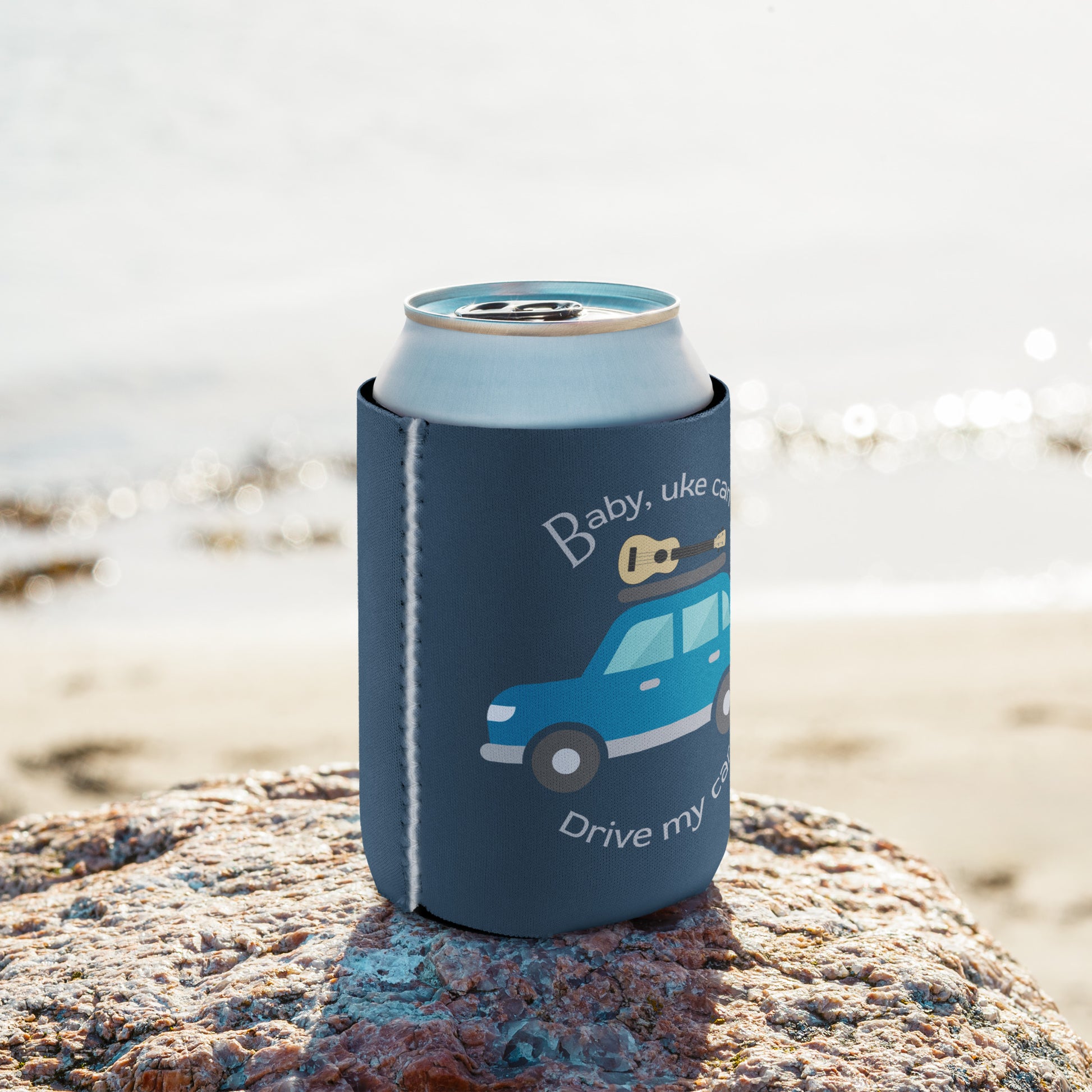 Regular-sized can coozie printed with an indigo background and ‘Baby, uke can drive my car’ with a graphic of a car with a ukulele on the roof.
