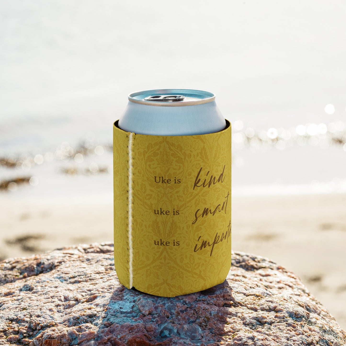 Regular-sized can coozie with a mustard-colored, patterned background and 'Uke is kind, uke is smart, uke is important' printed on it.