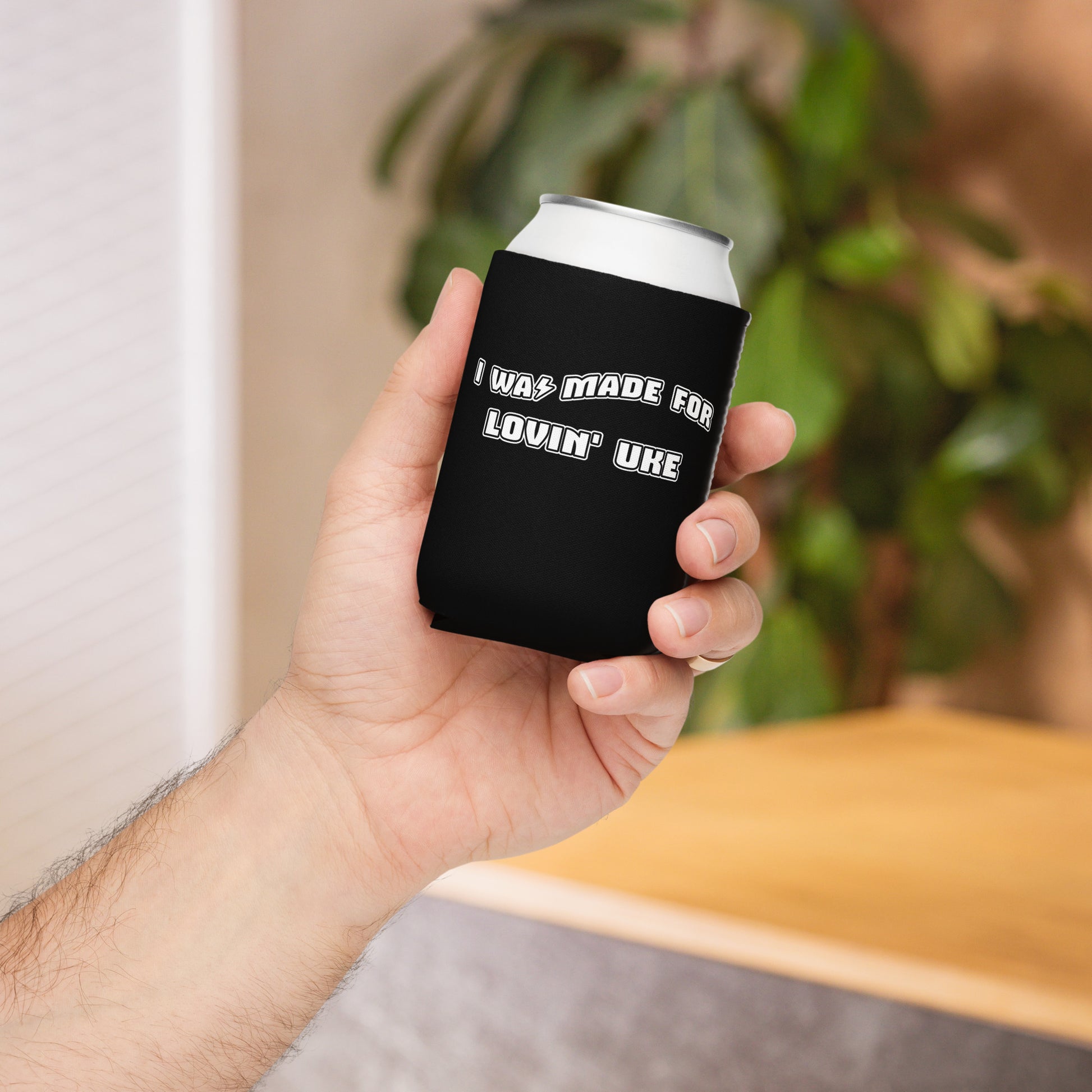Hand holding a regular-sized can coozie with a black background and 'I was made for lovin' uke' printed in black and white block letters.
