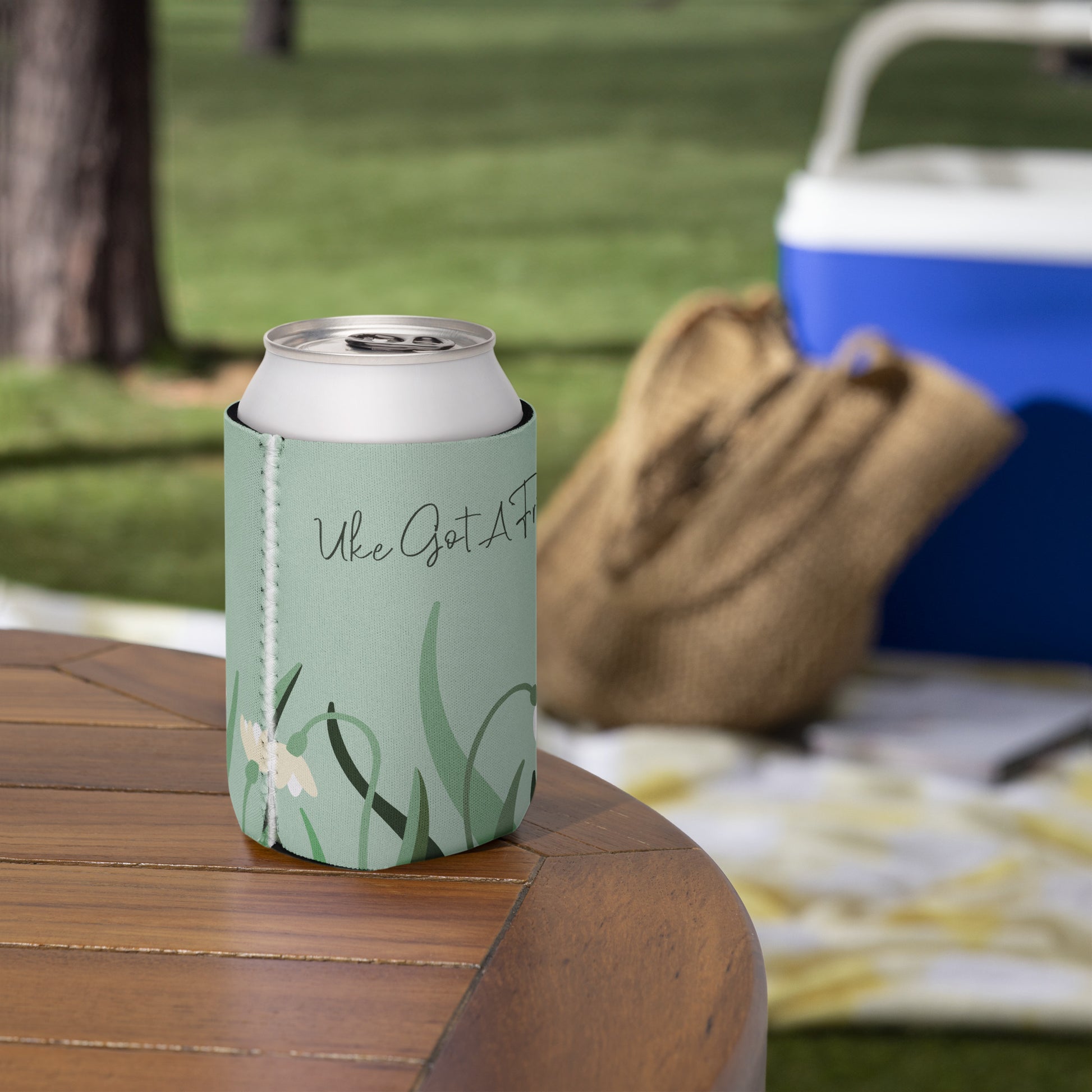 A regular-sized can coozie with a flower design on a green background and the words 'Uke Got A Friend' printed on it.