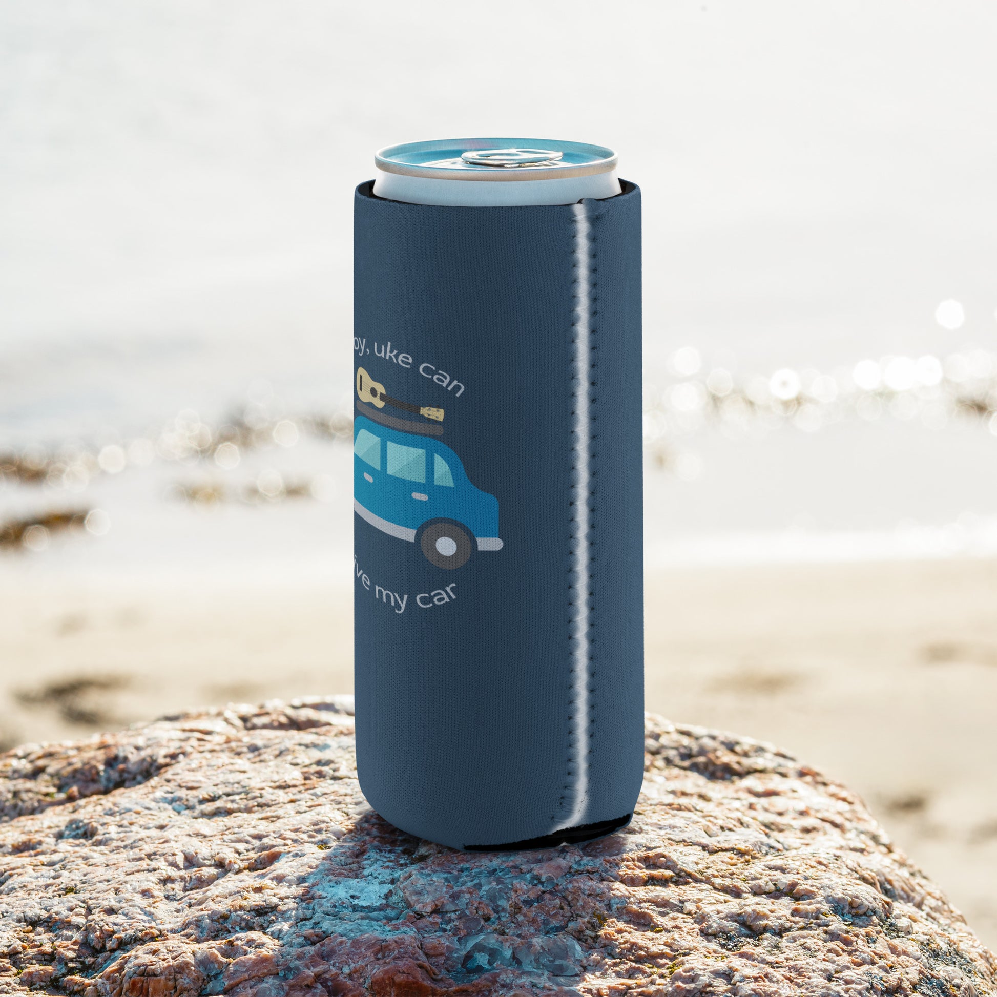 Slim can coozie printed with an indigo background and ‘Baby, uke can drive my car’ with a graphic of a car with a ukulele on the roof.