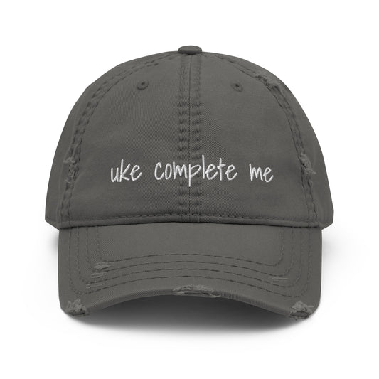 Grey baseball cap with a distressed look and 'Uke complete me' embroidered on it with white thread.