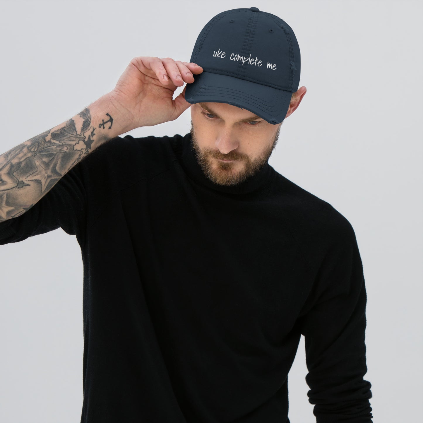 Man wearing a navy blue distressed baseball cap with 'uke complete me' embroidered in white thread.