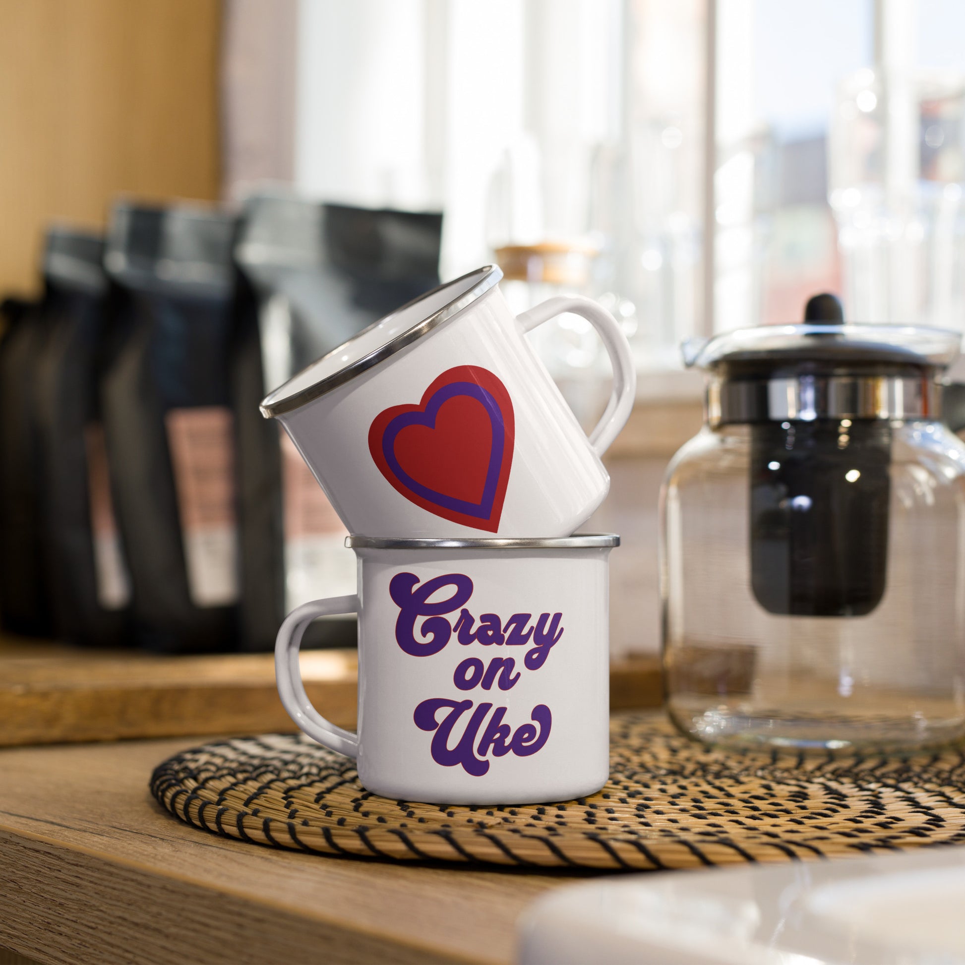 A stack of two white enamel mugs showing what both sides of a single mug look like. One side has a red and purple heart and the other side has red and purple bold cursive letters that say 'Crazy On Uke.’
