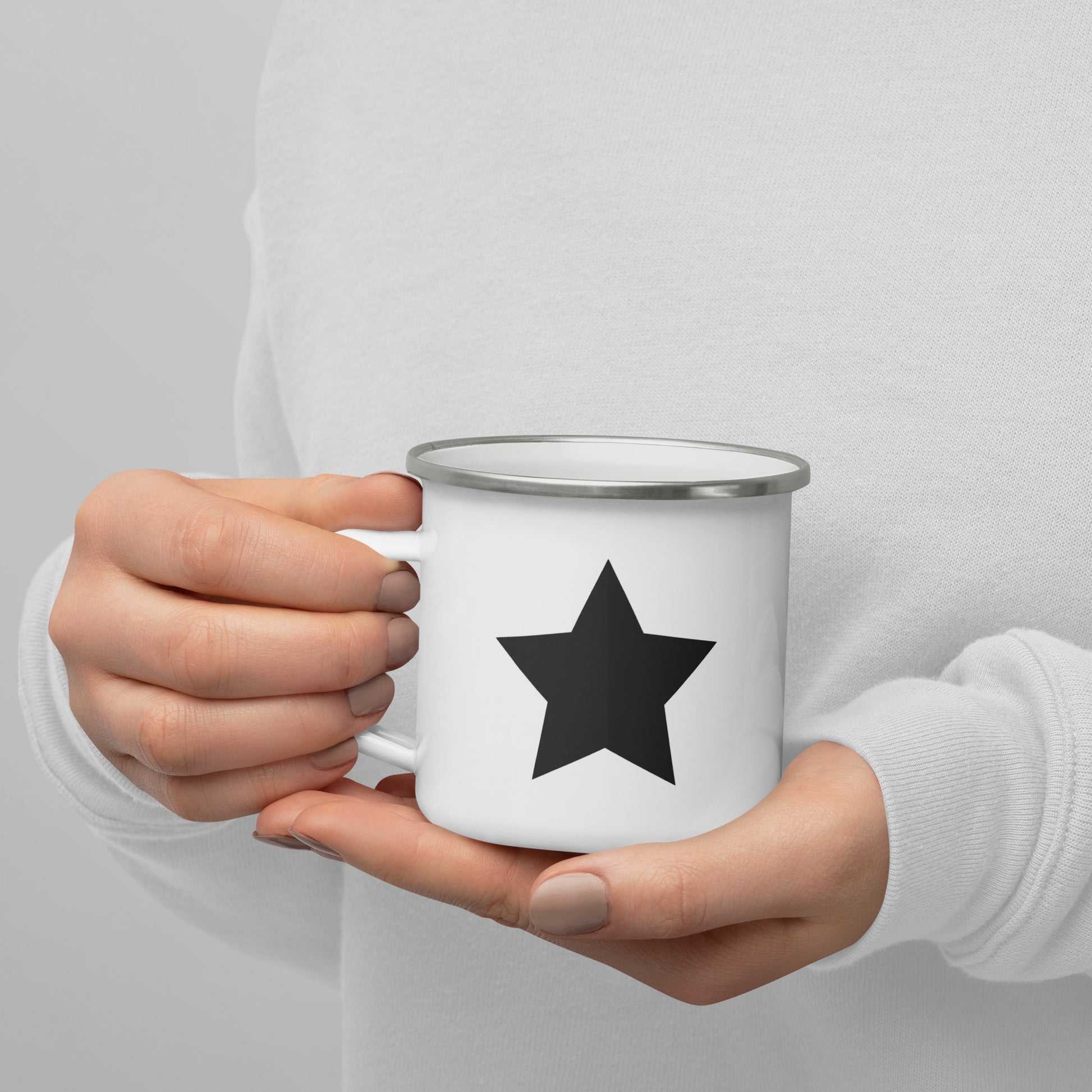 A person holding a white enamel mug with a black star printed on the right side of the handle.