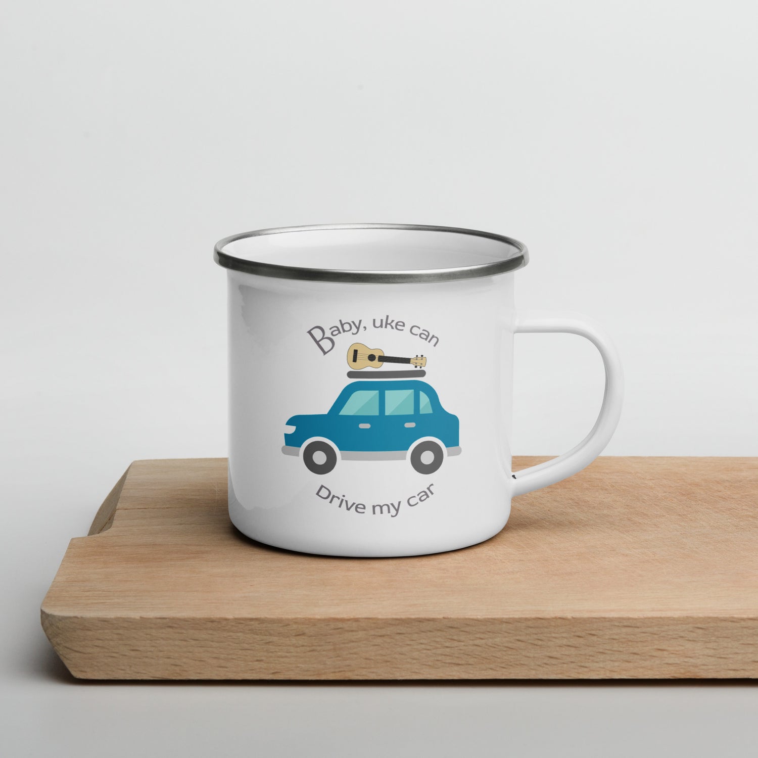 White enamel mug with ‘Baby, uke can drive my car’ and a graphic of a car with a ukulele on the roof printed on the side to the left of the mug handle.
