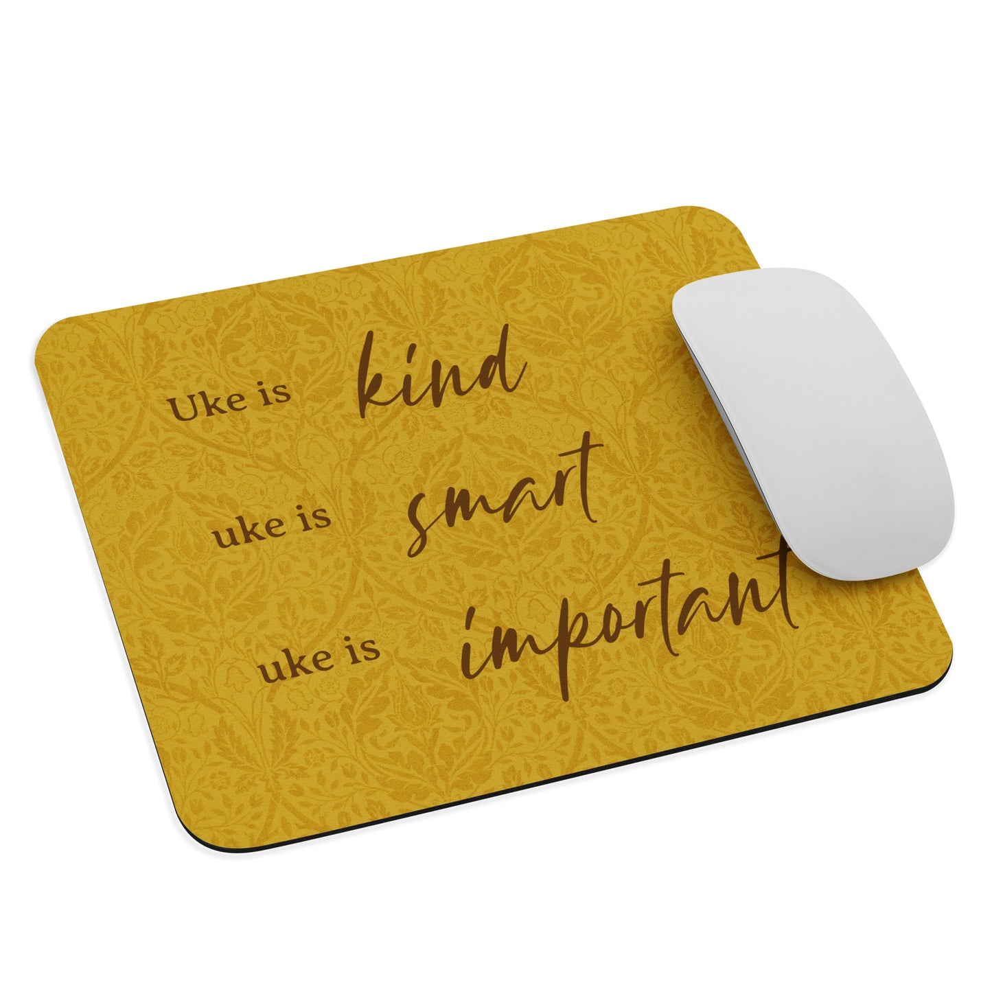 Mousepad with a mustard-colored, patterned background and 'Uke is kind, uke is smart, uke is important' printed on it, with a mouse sitting on top of it.