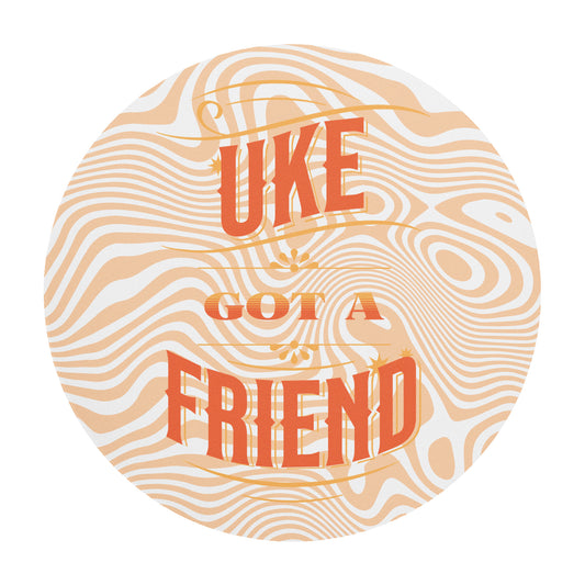 Round mouse pad with 'Uke Got A Friend' printed on it in orange and yellow block letters with a swirly design in the background.