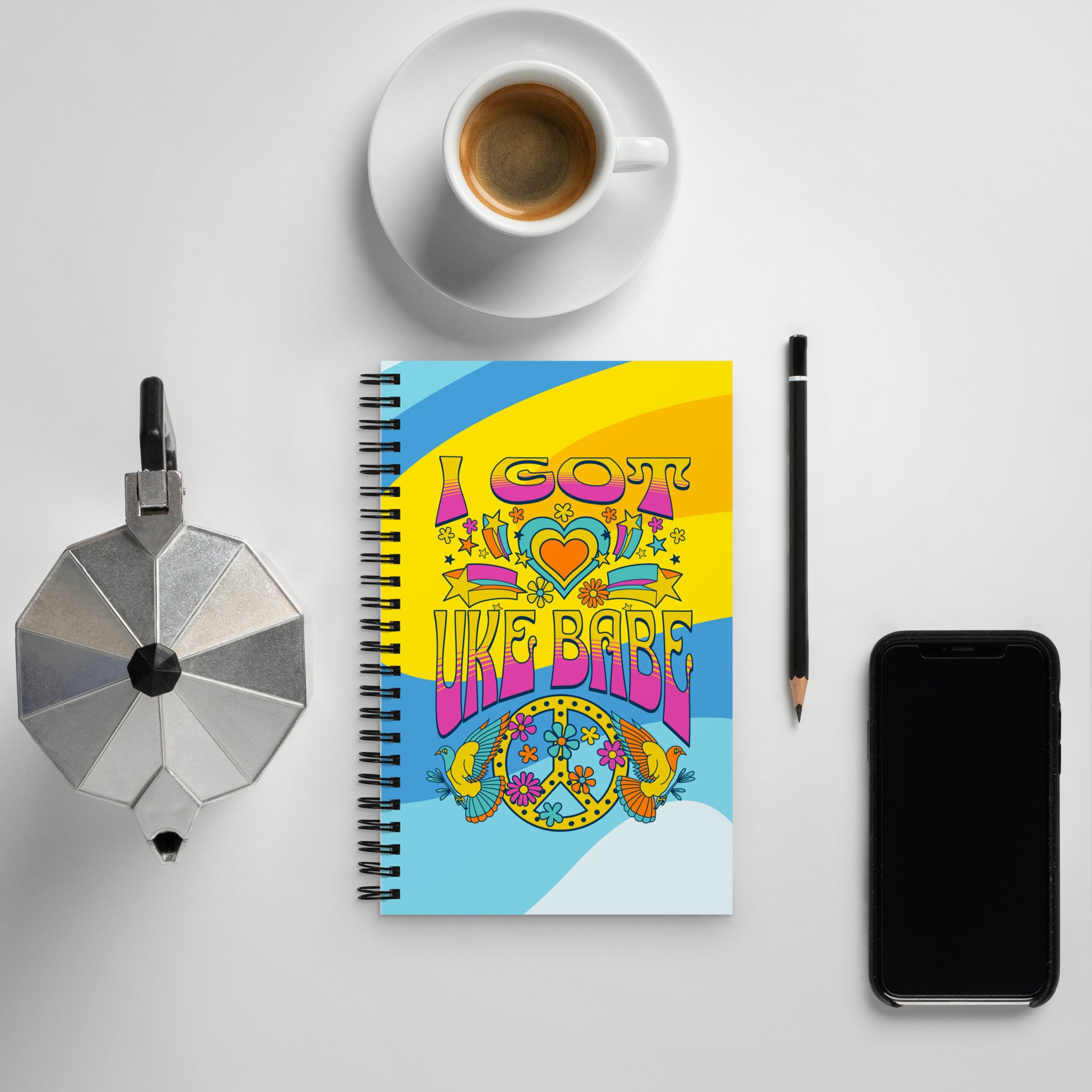 A 5-by-7 inch notebook with 'I Got Uke Babe' and a blue, pink, and yellow peace sign graphic printed on a swirly blue and yellow background.
