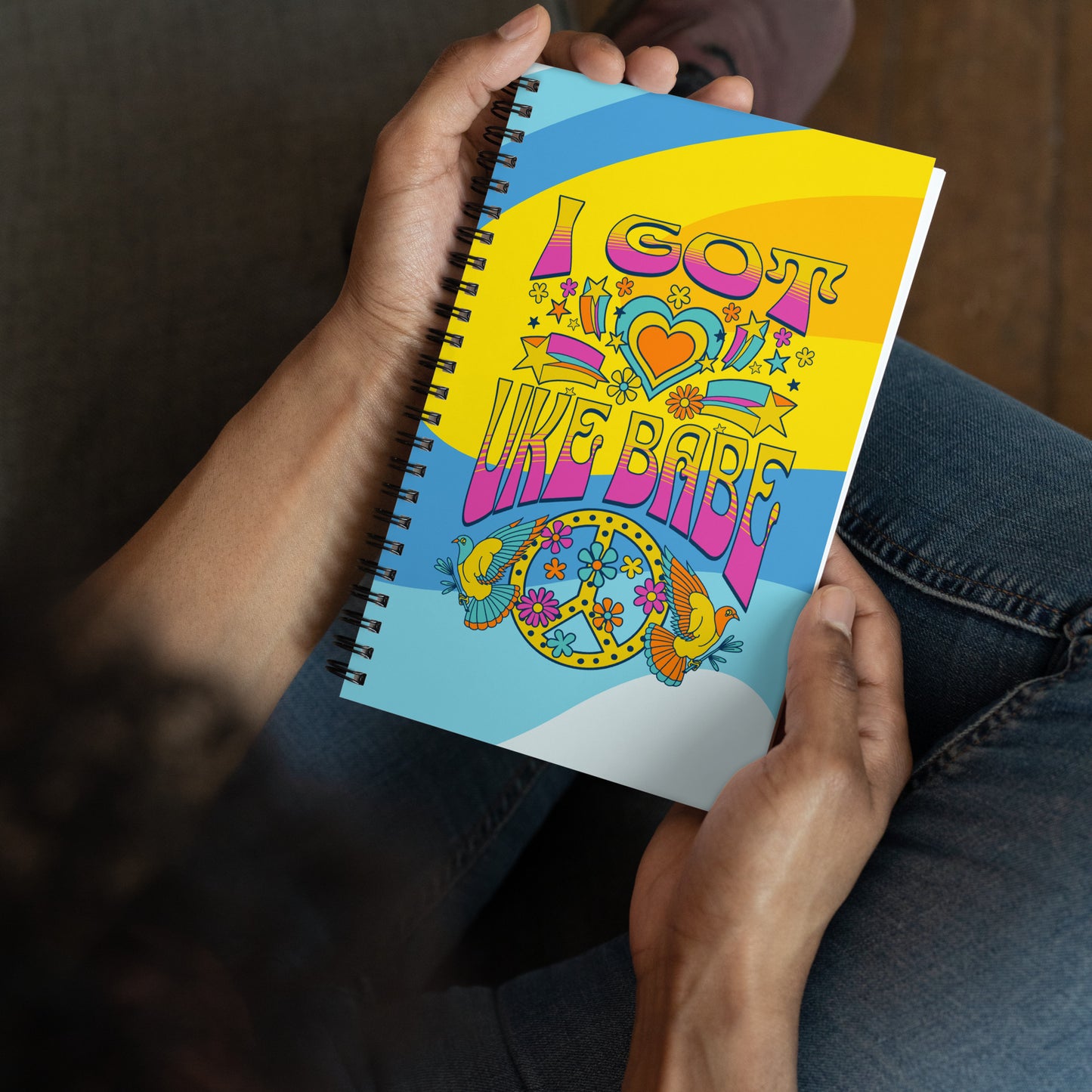 Hands holding a 5-by-7 inch notebook with 'I Got Uke Babe' and a blue, pink, and yellow peace sign graphic printed on a swirly blue and yellow background.