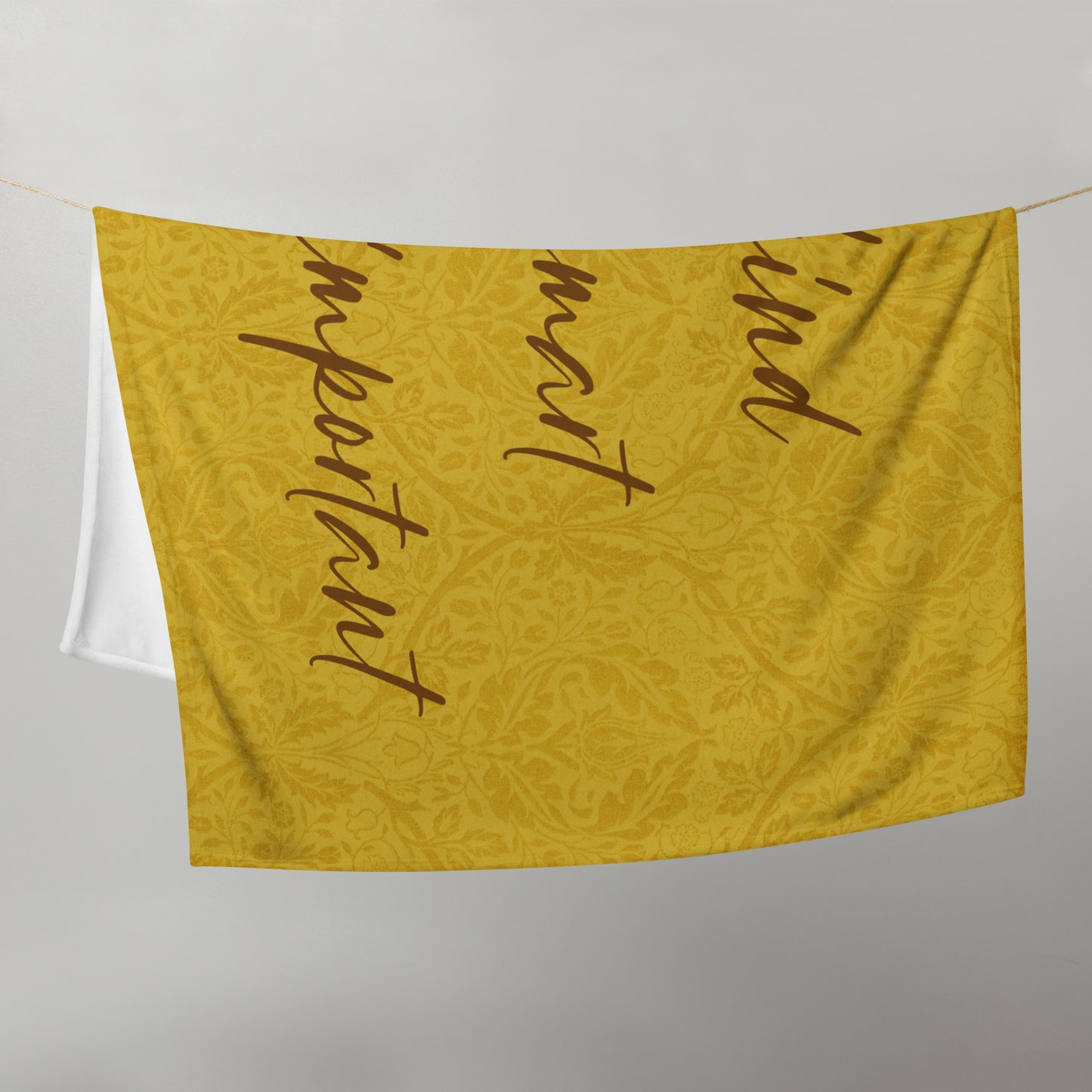Microplush throw blanket with a mustard-colored, patterned background and 'Uke is kind, uke is smart, uke is important' printed on it, draped over a clothesline.