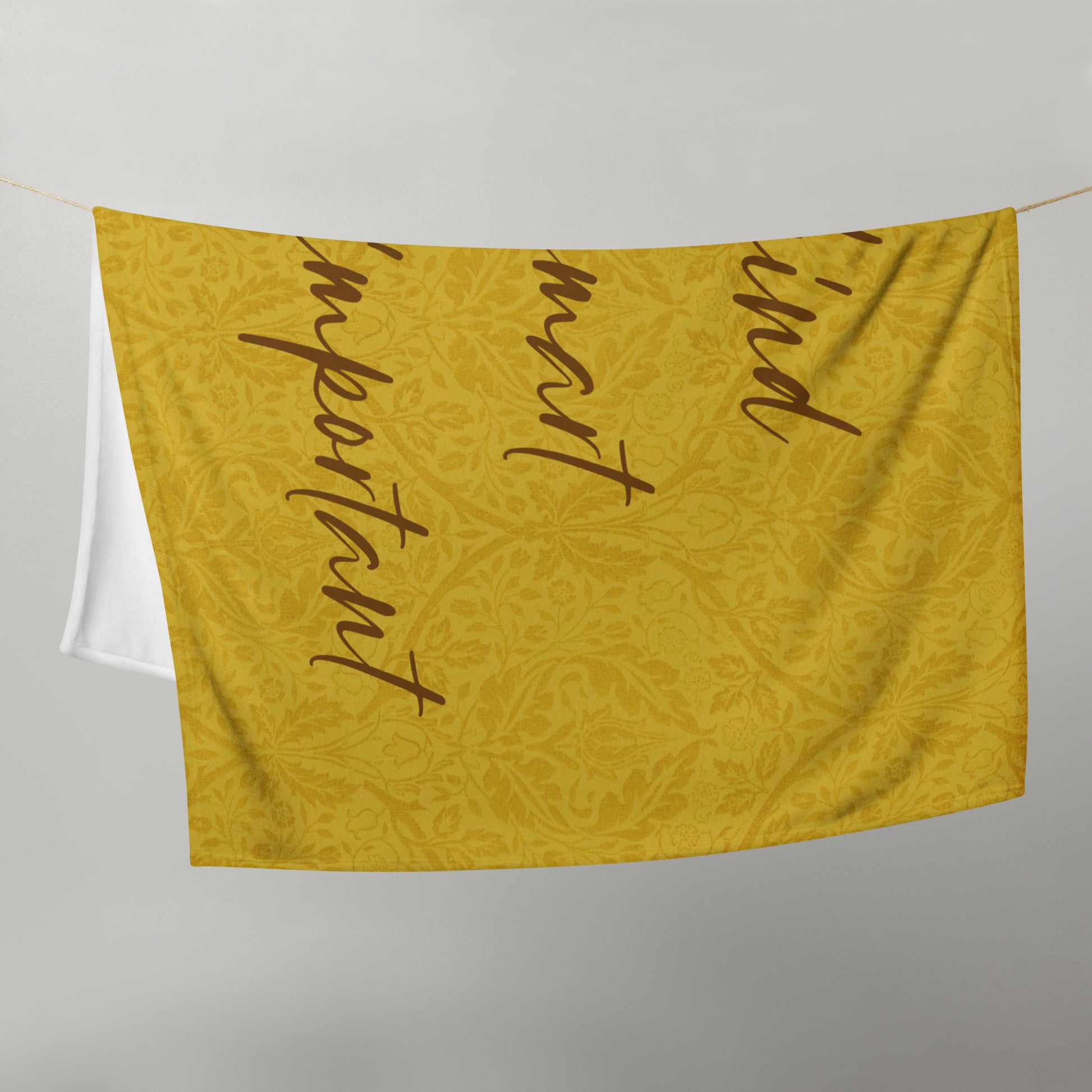 Microplush throw blanket with a mustard-colored, patterned background and 'Uke is kind, uke is smart, uke is important' printed on it, draped over a clothesline.