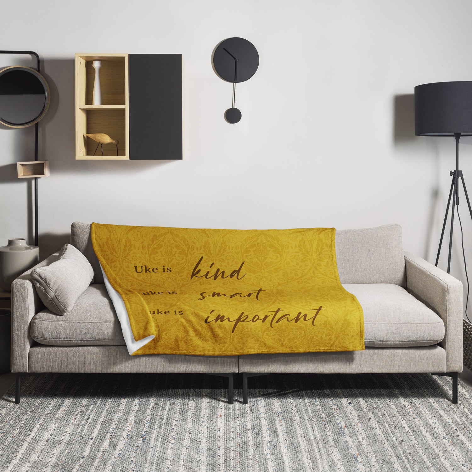 Microplush throw blanket with a mustard-colored, patterned background and 'Uke is kind, uke is smart, uke is important' printed on it, draped over a sofa.
