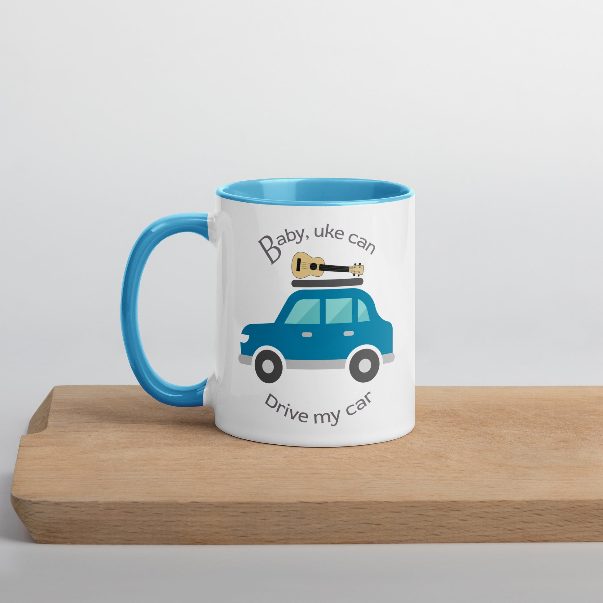 White mug with light blue handle and inside, with ‘Baby, uke can drive my car’ and a graphic of a car with a ukulele on the roof printed on the side to the right of the handle.