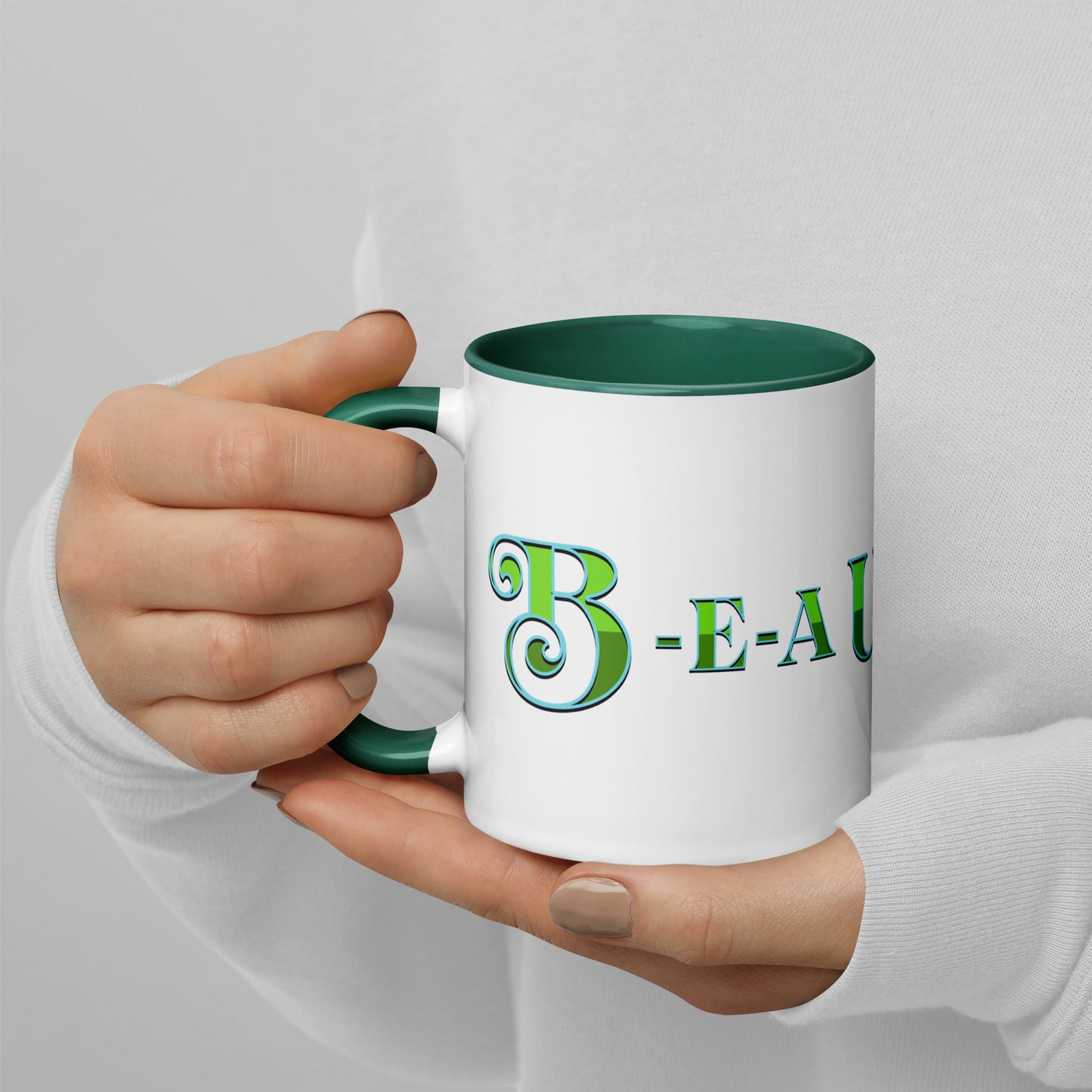 Person holding a white mug with dark green handle and inside, with ‘B-E-A-UKE-tiful’ printed across the mug from one side of the handle to the other.