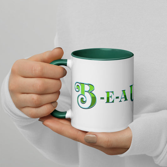 Person holding a white mug with dark green handle and inside, with ‘B-E-A-UKE-tiful’ printed across the mug from one side of the handle to the other.