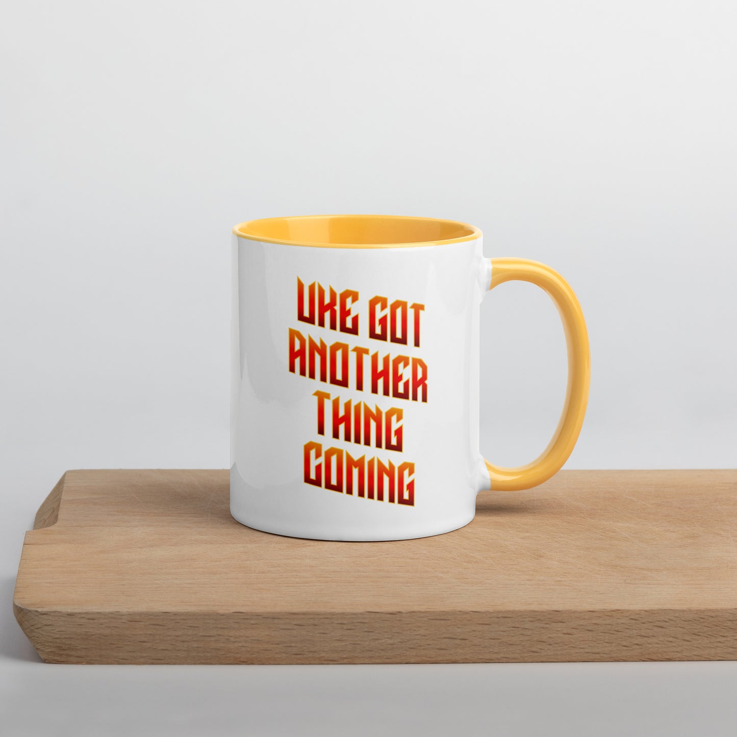 White mug with yellow handle and inside, with ‘Uke Got Another Thing Coming' in orange and yellow slanted block letters printed on the side to the left of the handle.