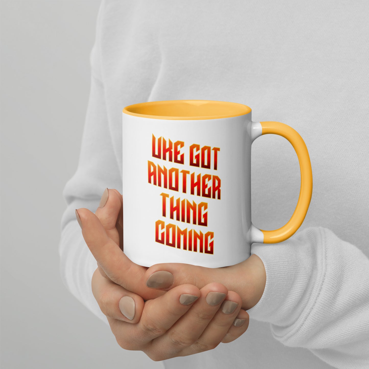 White mug with yellow handle and inside, with ‘Uke Got Another Thing Coming' in orange and yellow slanted block letters printed on the side to the left of the handle.