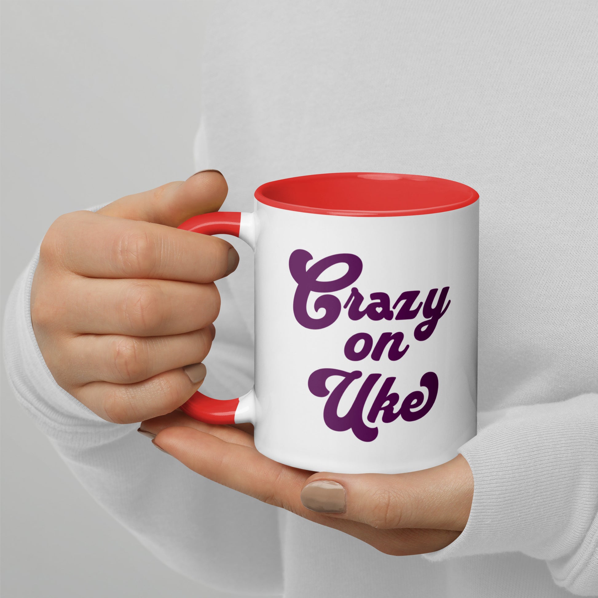 White mug with red handle and interior, with 'Crazy On Uke' in purple cursive text printed on the side to the right of the handle.