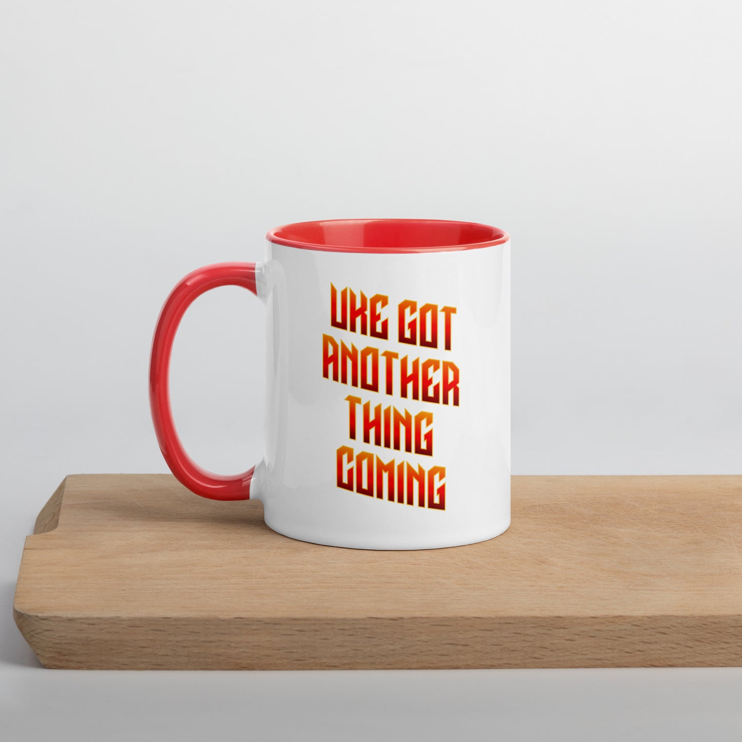 White mug with red handle and inside, with ‘Uke Got Another Thing Coming' in orange and yellow slanted block letters printed on the side to the right of the handle.