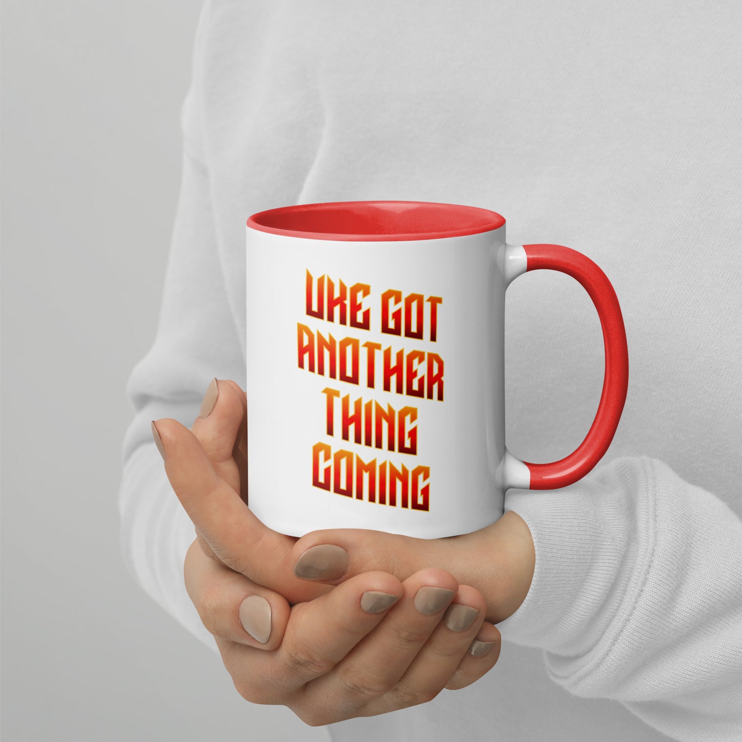 White mug with red handle and inside, with ‘Uke Got Another Thing Coming' in orange and yellow slanted block letters printed on the side to the left of the handle.