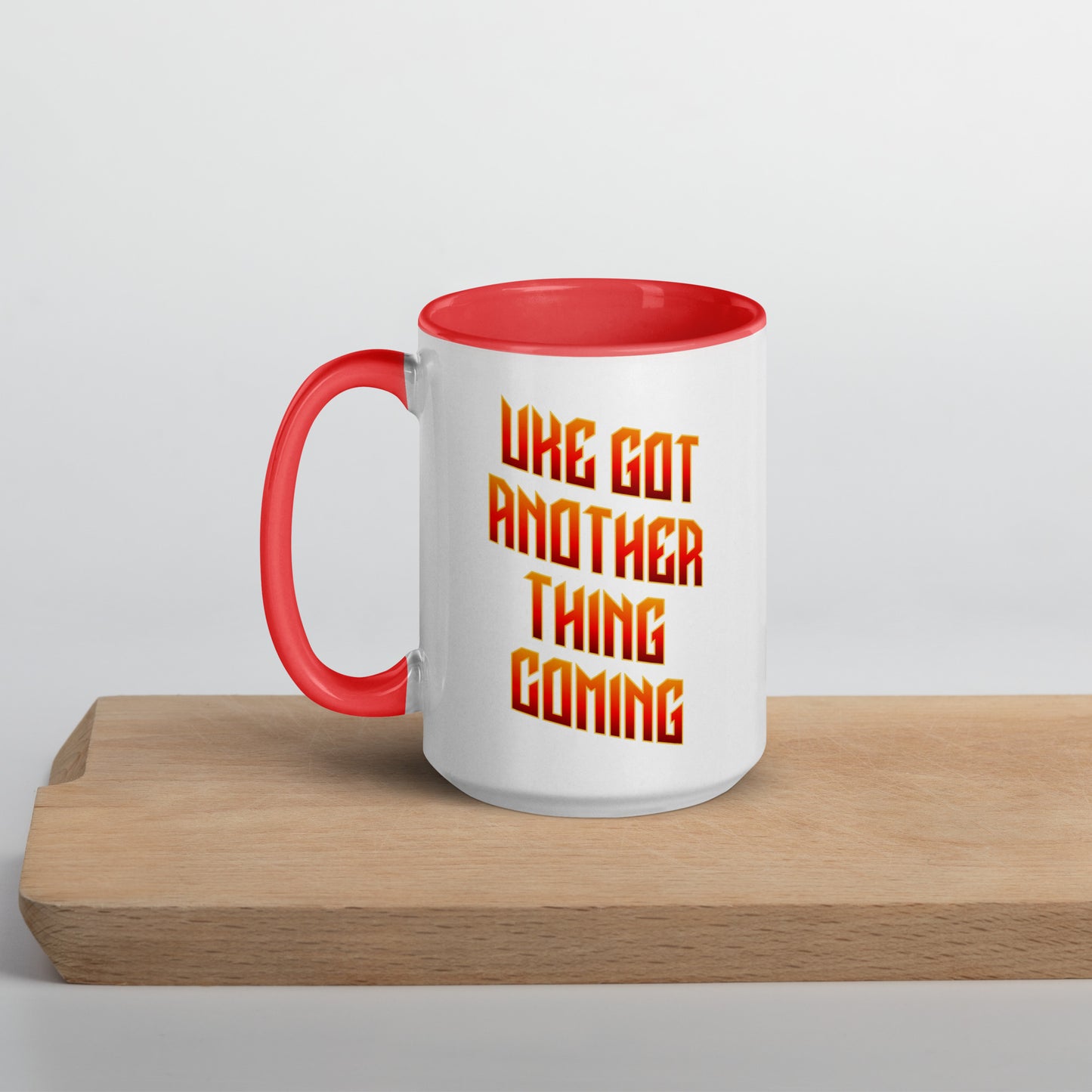 White mug with red handle and inside, with ‘Uke Got Another Thing Coming' in orange and yellow slanted block letters printed on the side to the right of the handle.