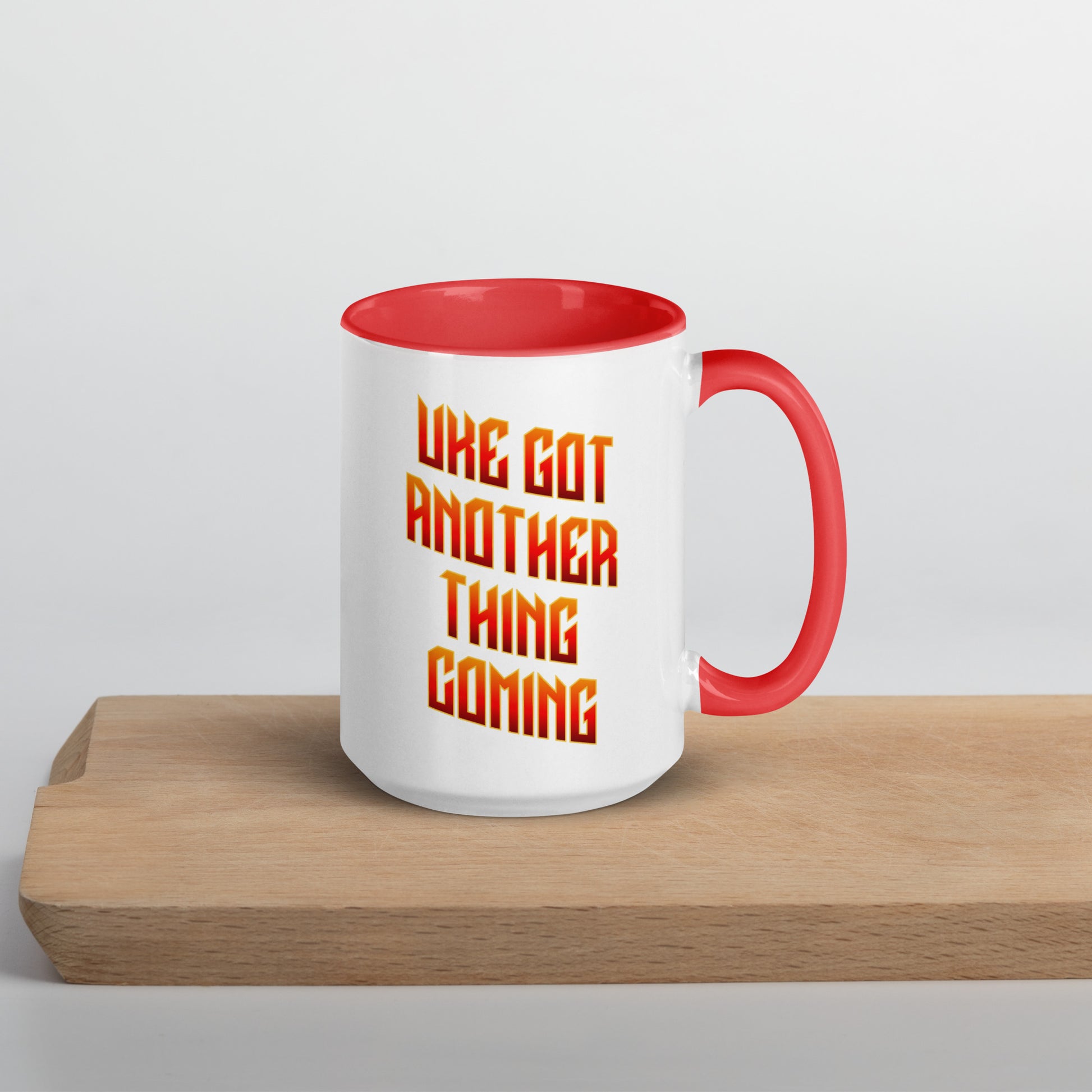 White mug with red handle and inside, with ‘Uke Got Another Thing Coming' in orange and yellow slanted block letters printed on the side to the left of the handle.
